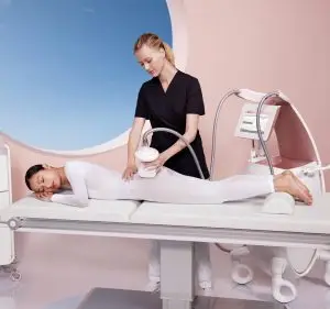 Endermologie specialist applying body sculpting device to woman lying on table