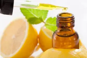 Lemon Essential Oil being dropped into a bottle with lemonds in background.