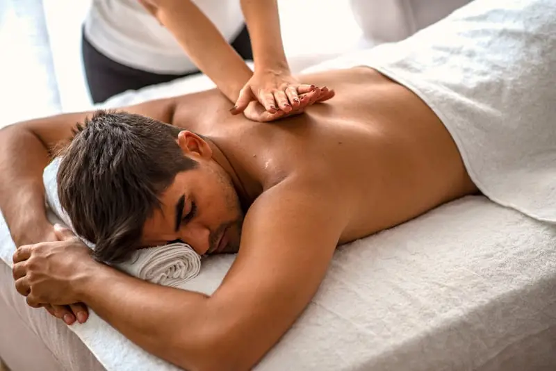 Massage therapist applying pressure to man's upper back.